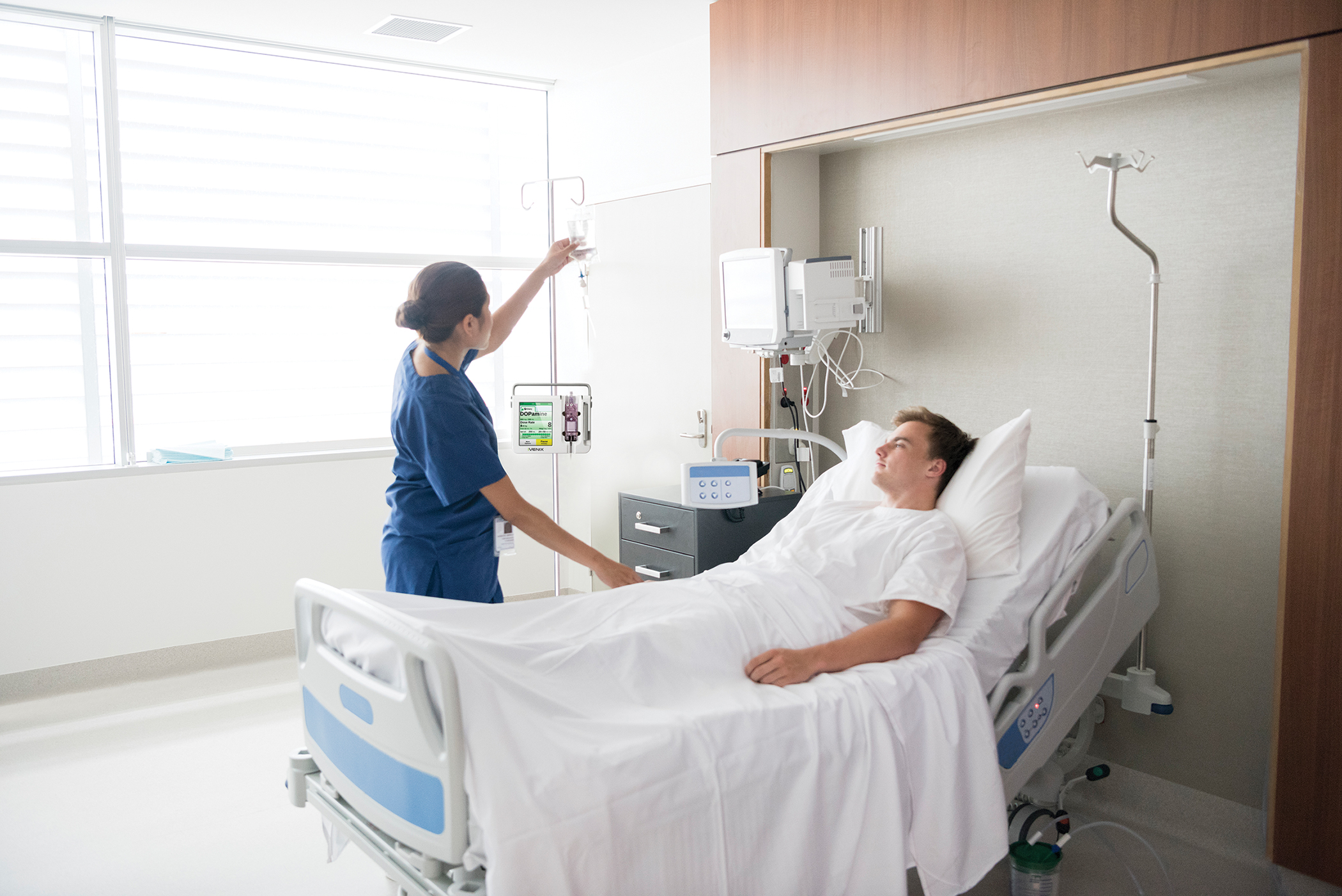 Female Nurse Tending To Male Patient In Hospital Bed Patient Safety And Quality Healthcare